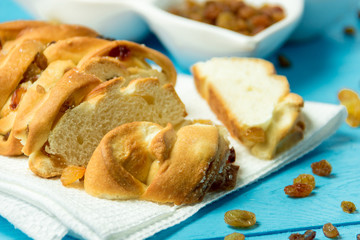 Piece of Sweet Braided Bread with raisins on kitchen towel on blue wooden background.