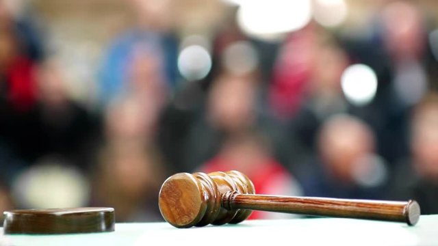auctioneer or judge gavel mallet in foreground focused with public or jury in background unfocused , HD video footage