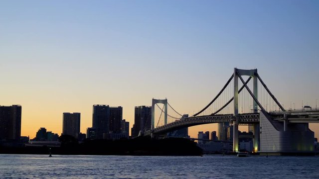Time lapse view of cityscape from sunfall to night with water front and a  rainbow bridge at tokyo japan