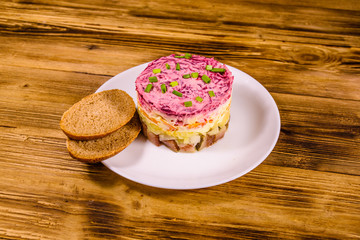 White plate with russian traditional new year salad herring under fur coat and rye bread on wooden table