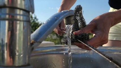Young woman s hands scouring a long skewer over outdoor sink in summer in slo-mo