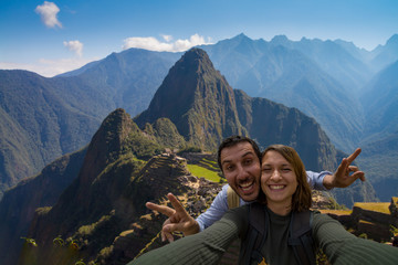 Happy couple backpackers traveling in front of Machu Picchu. taking selfie in front of the ruins of the ancient city. Cusco, Peru travel