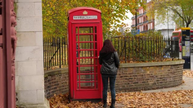 4k woman uses a red phone booth in London England UK