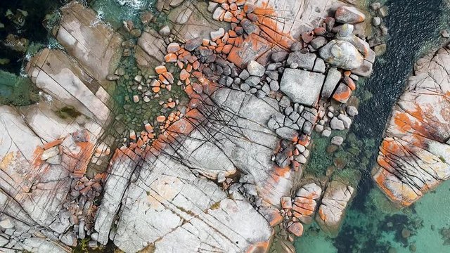Aerial of Bay of Fires bright orange rocks with waves in rock pools in the sea. Binalong Bay, Tasmania, Australia