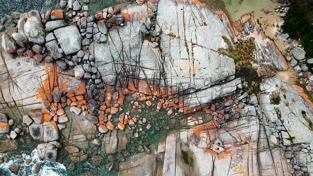 Aerial of Bay of Fires bright orange rocks with waves in rock pools in the sea. Binalong Bay, Tasmania, Australia
