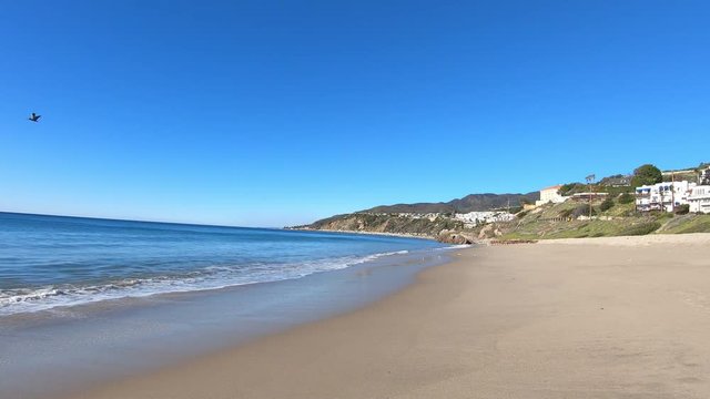 Waves breaking gently on Malibu beach, view of city on coastline and ocean
