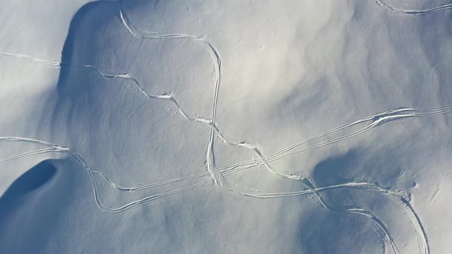 Aerial shot looking down on fresh snow with ski tracks while flying along in sun shine. In the French Alps in winter.