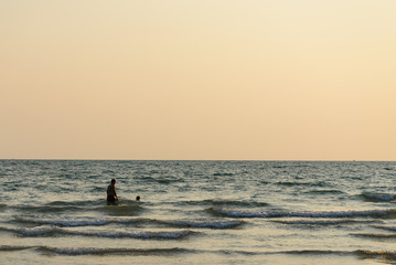 Fototapeta premium Silhouette scenery father and son stand on coast enjoy and have fun with wave from sea during sunset time with dusk sky. Holiday, vacation feeling on the sea in evening. 