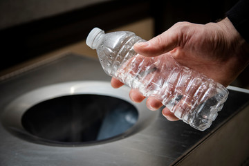 Hand throwing disposable plastic water bottle into trash or recycling bin.