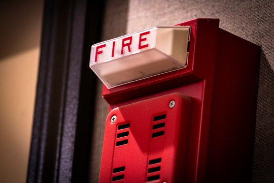 Red fire alarm/detector/siren/light system component on wall of school or workplace.