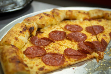 Slices of greasy American pepperoni pizza on a restaurant pizza pie pan.