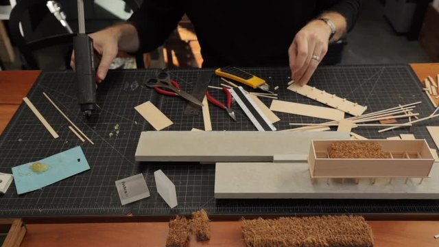 Male architect gluing and constructing a scale model of a modern residence on a work table in his design studio.