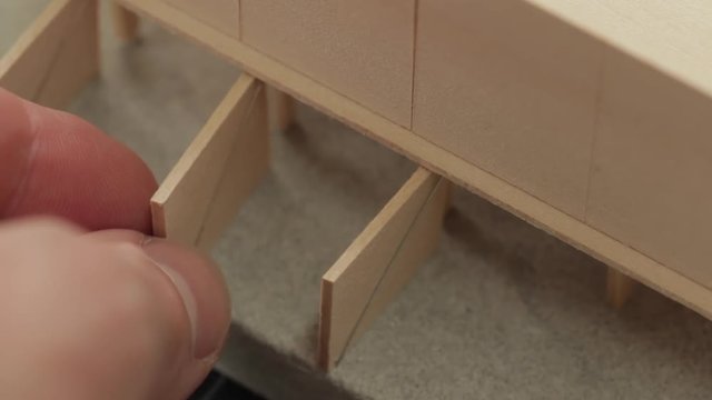 Extreme close up of architect's hands placing a door on a wood scale model of a modern home design.