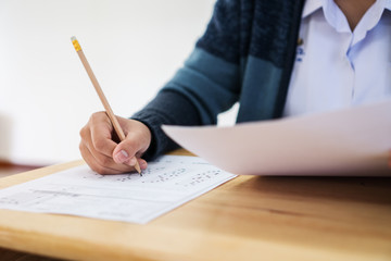 Students hands taking exams, writing examination room with holding pencil on optical form of standardized test with answers and english paper sheet on row desk chair doing final exam in classroom.