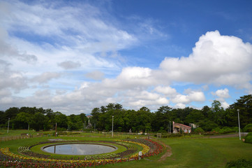 Fototapeta na wymiar 円形の大きな花壇と芝生の広場がある公園の上空に青空と夏の雲が広がっている風景