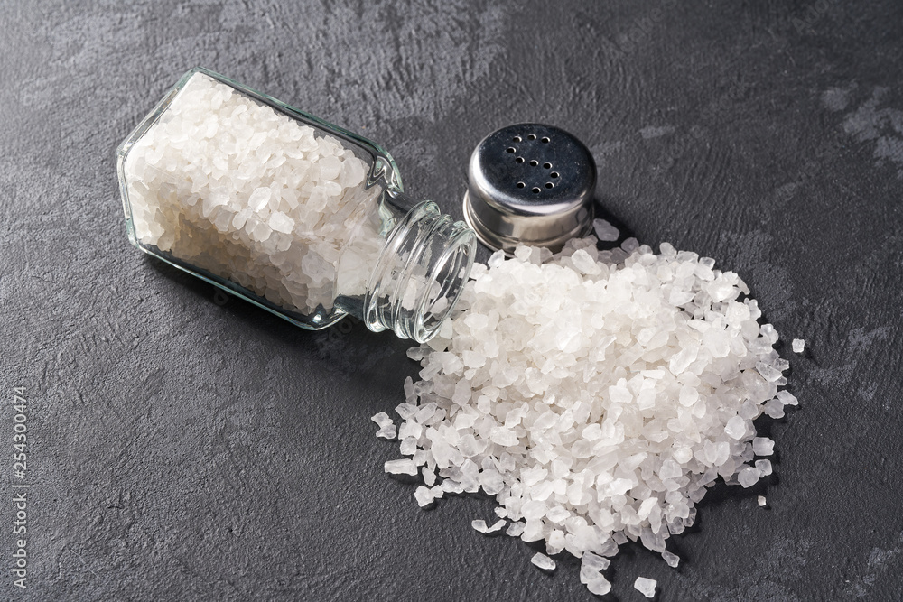 Wall mural salt shaker with spilled salt on black stone background, top view.