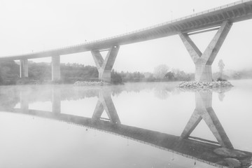 concrete bridge with fog in black and white crossing the river