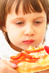 Cute child girl is eating a piece of pizza.