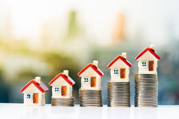 Concept for property ladder, mortgage and real estate investment. House models on top of coins stack with city backgrounds.