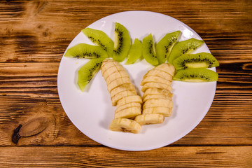Healthy fruit dessert for children with kiwi and bananas shaped as a palm tree on white plate