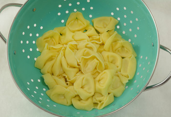 Close up of boiled cheese tortelloni draining in blue colander on white background