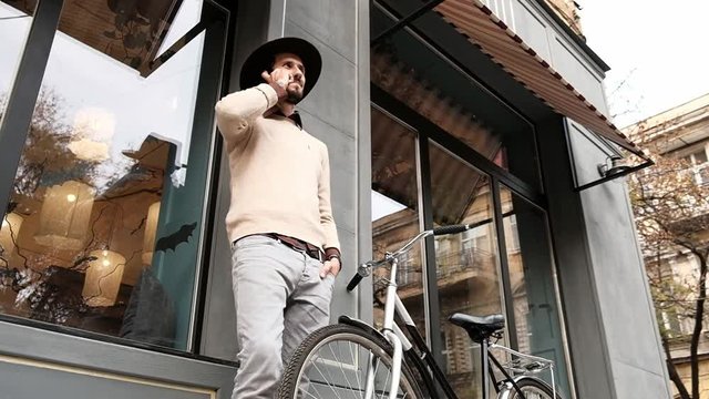 Stylish young bearded man with bicycle answering phone call