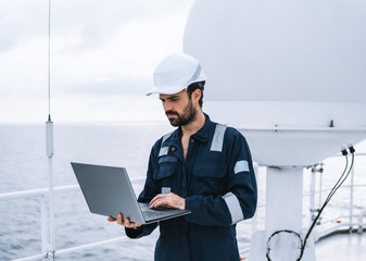 Marine service technician or serviceman near VSAT terminal on deck of vessel or ship. He is working...