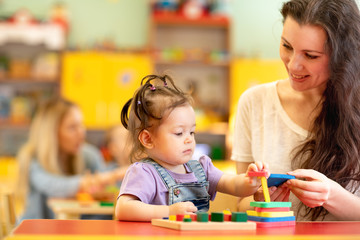 Babies with teachers playing with developmental toys in nursery