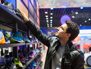 portrait of young male customer choosing sneakers at supermarket store. He is taking shoes from she...
