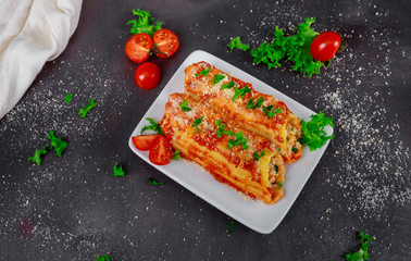 Baked cannelloni with cheese, tomatoes on a white dish plate