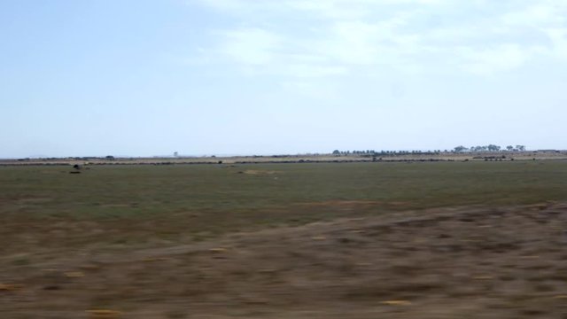 View from a train window look out at dry arid farm land. Blue sky and cloud.