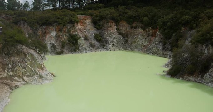 From bottom to top shot of Wai-O-Tapu Thermal Wonderland, New Zealand, a light green geothermal pool with trees in the background, on a sunny day with some clouds