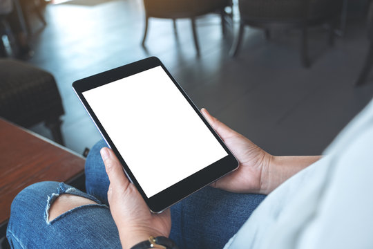 Mockup image of a woman sitting and holding black tablet pc with blank white desktop screen