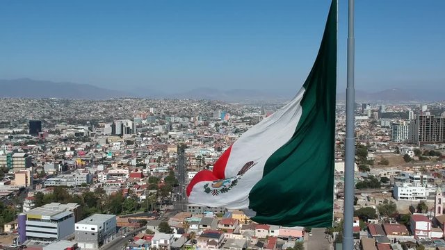 Sweeping Aerial Shot Of The Mexican Flag Waving Over Tijuana.