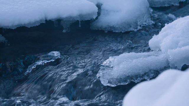 Slow motion close up shot of a small stream flowing in winter with chunks of ice and snow surrounding it