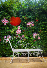 Fototapeta na wymiar Vintage bench or chair with flower plant and red heart on green nature wall background