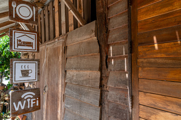 Fototapeta na wymiar Signs hanging in front of an old wooden homestay indicating food, accommodation, coffee, and free wifi available at Maekampong village in Chiang Mai, Thailand.