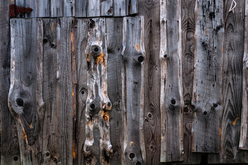 A wall made of old, darkened, frayed gray wooden knotty planks.