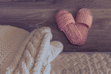 Cozy knitted slippers beside the bed. Night bedroom. White knitted plaid on the bed.
