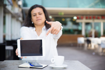 Serious woman pointing at tablet computer screen in street cafe