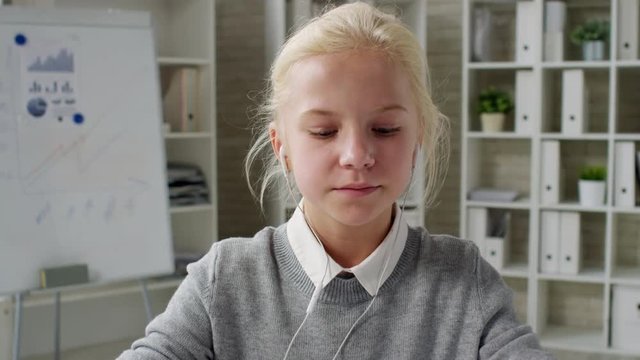 Lockdown of Caucasian blonde girl sitting with headphones in her ears, talking with her business partner about chart in her hands via internet