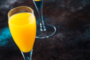 Low alcohol cocktail mimosa with orange juice and cold dry champagne or sparkling wine in glasses, blue background with flowers, place for text, selective focus