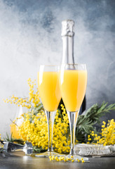 Festive alcohol cocktail mimosa with orange juice and cold dry champagne or sparkling wine in glasses, gray bar counter background with flowers, place for text, selective focus