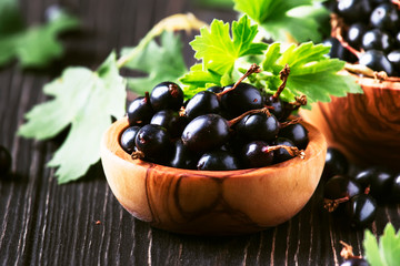 Shining fresh black currants in wooden bowls, summer harvesting, black kitchen table background, place for text, selective focus