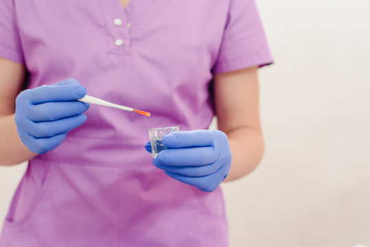 Female hands of a beautician with small glass cup and aplicator