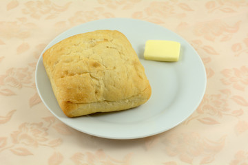 Ciabatta roll with pad of butter on white bread plate on tablecloth © merrimonc