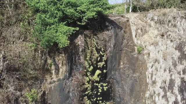 Aerial shot, medium shot, of a waterfal crest, very little water sprinking down and Black vultures flying away, Meseta de Chorcha, Chiriqui, Panama