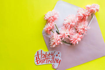 Festive flower composition, invitation on craft envelope ,yellow background. top view.Happy Birthday postcard.spring composition. a bouquet of chrysanthemums in envelope. postcard design.Copy space