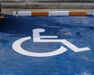Handicap symbol on road, traffic and pedestrians in background. Parking for disabled people in gas...