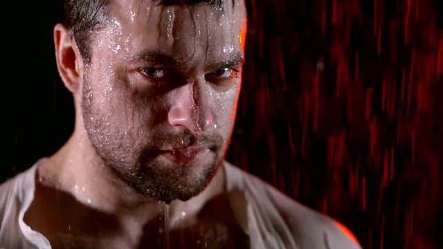 Close-up shot of a brutal guy in a white shirt standing under the rain.